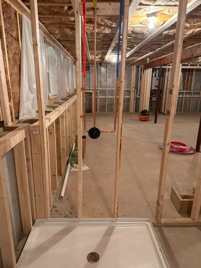 Basement bathroom shower rough-in with PEX water lines, copper piping, and a shower pan installed.