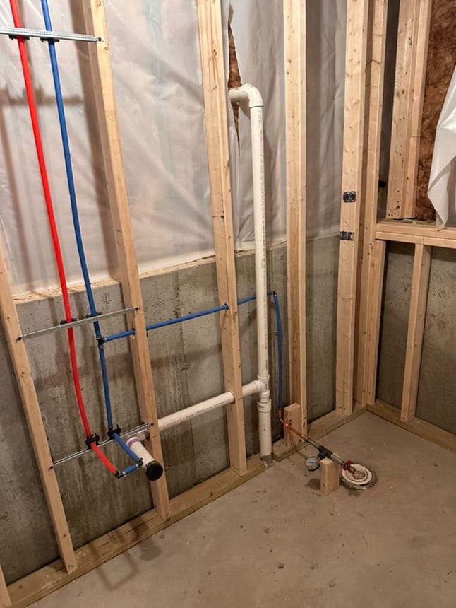 Residential bathroom plumbing rough-in with PEX water lines and PVC drain pipes in a basement framing.