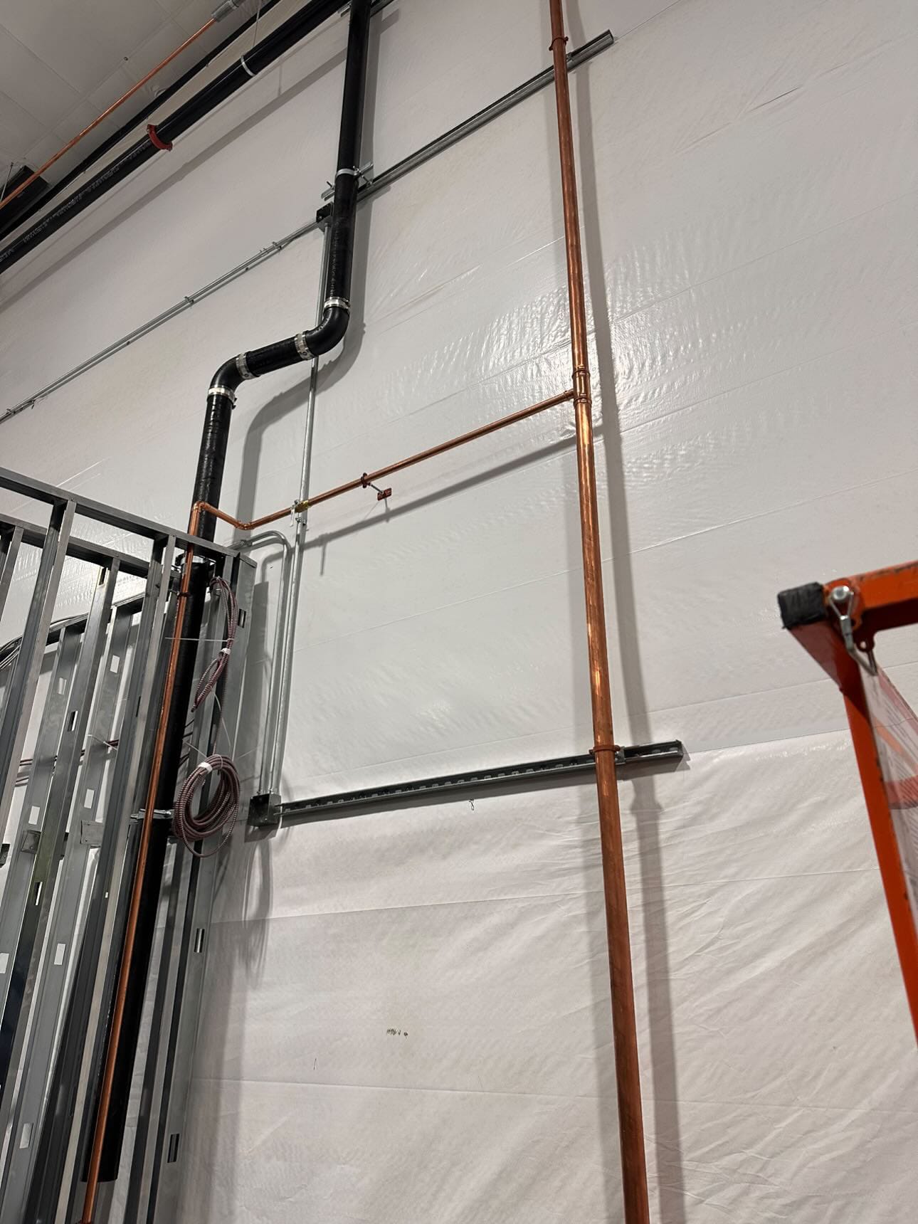 Commercial plumbing installation with copper and black iron piping along an insulated wall.