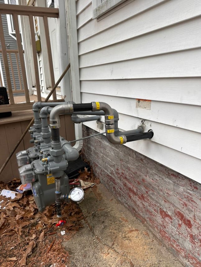 Residential gas meter installation with black iron and galvanized piping on an exterior brick foundation.