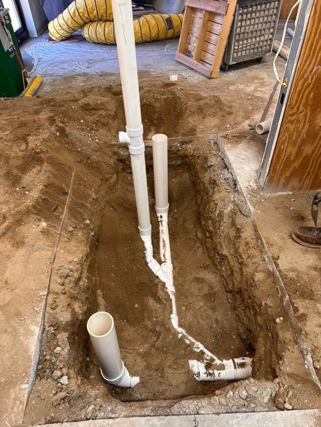 Commercial plumbing installation with underground PVC drainage pipes in a trench inside a building.