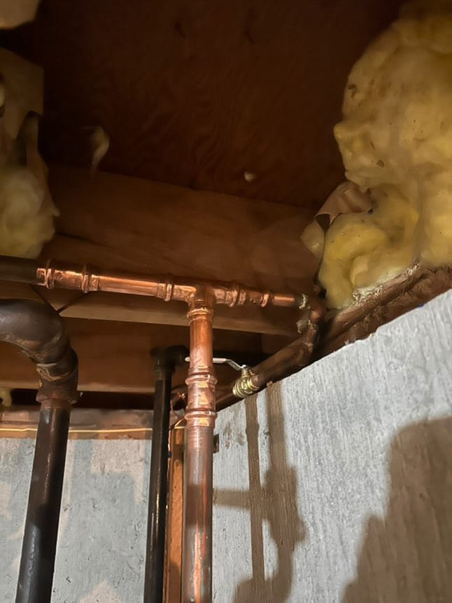 Newly installed copper and black iron piping in a basement ceiling with insulation.