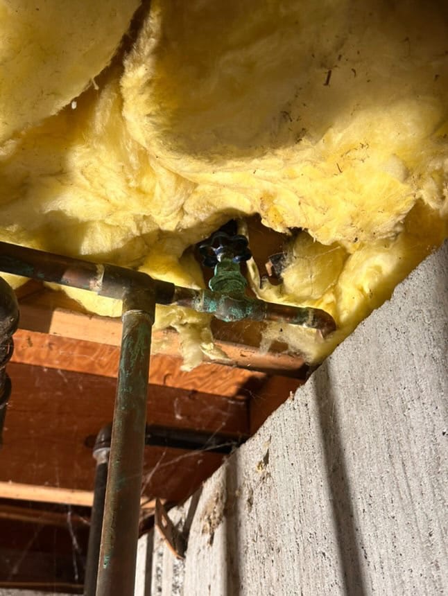 Corroded copper water valve with insulation damage in a basement ceiling.