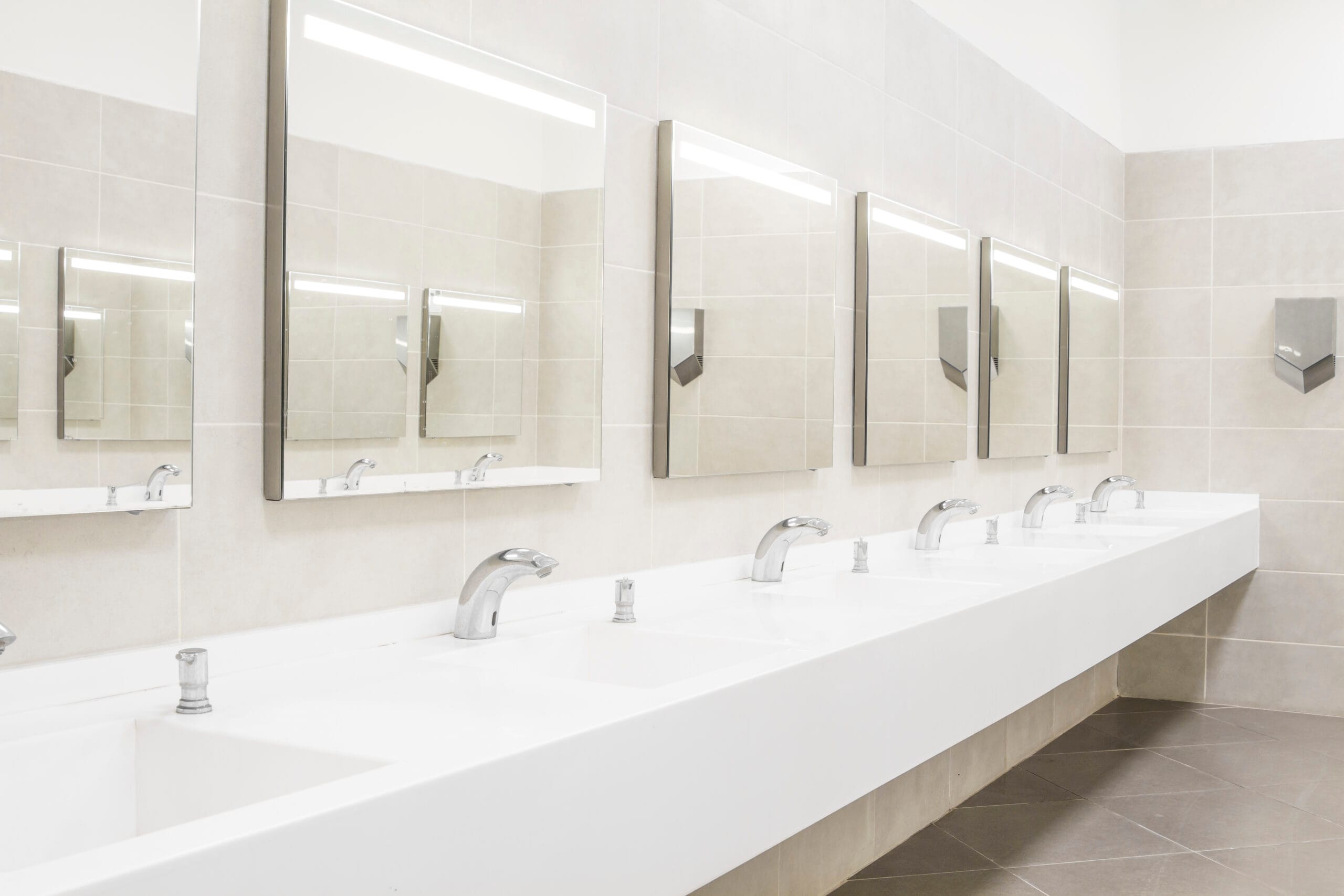 Modern commercial restroom with multiple sinks, mirrors, and touchless faucets, designed for high-traffic business and office buildings.