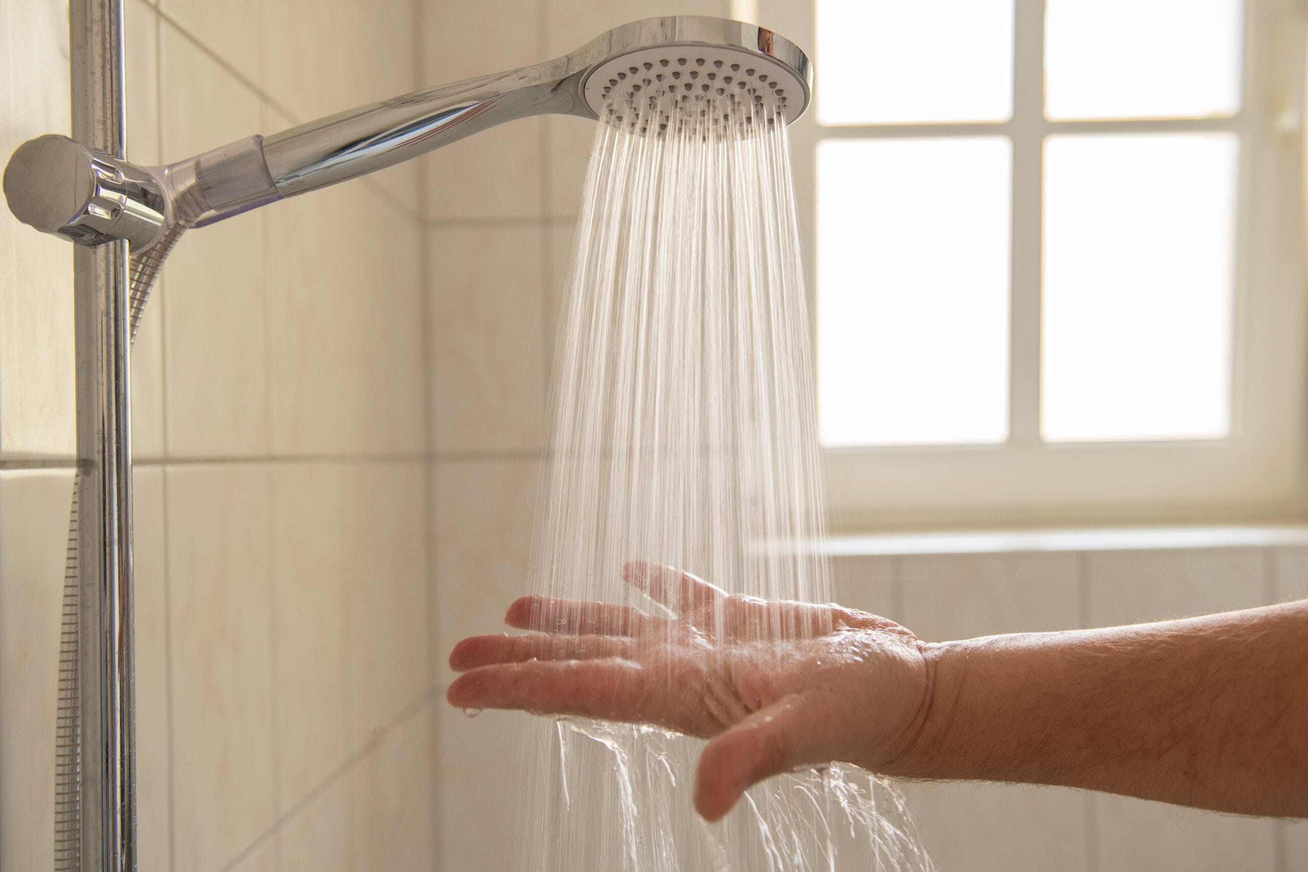 Person testing hot water flow from a handheld showerhead in a modern bathroom, ensuring proper water pressure and plumbing performance.